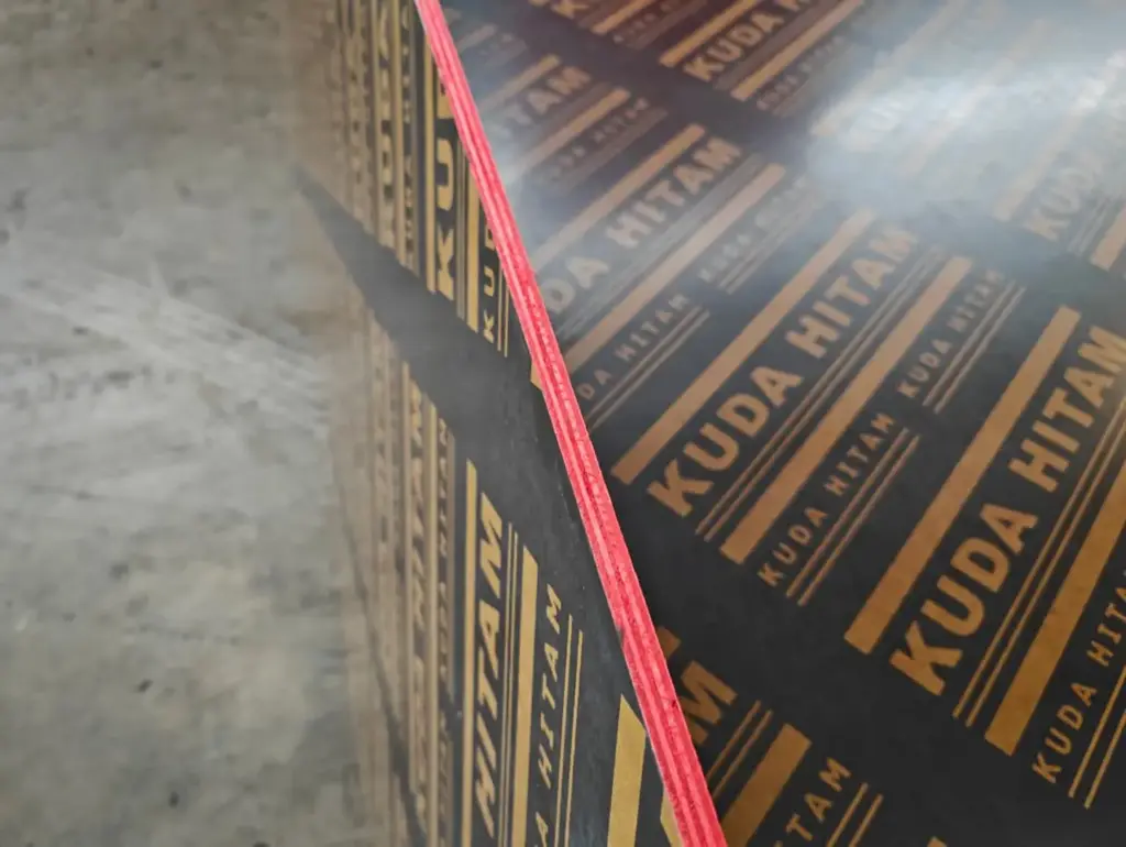 Detail lapisan Triplek Phenolic Film Face Kuda Hitam yang padat, menunjukkan ketebalan dan pinggiran yang dicat merah untuk melindungi dari air dan kelembapan. Plywood bekisting berkualitas tinggi dari Indoho.