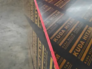 Detail lapisan Triplek Phenolic Film Face Kuda Hitam yang padat, menunjukkan ketebalan dan pinggiran yang dicat merah untuk melindungi dari air dan kelembapan. Plywood bekisting berkualitas tinggi dari Indoho.