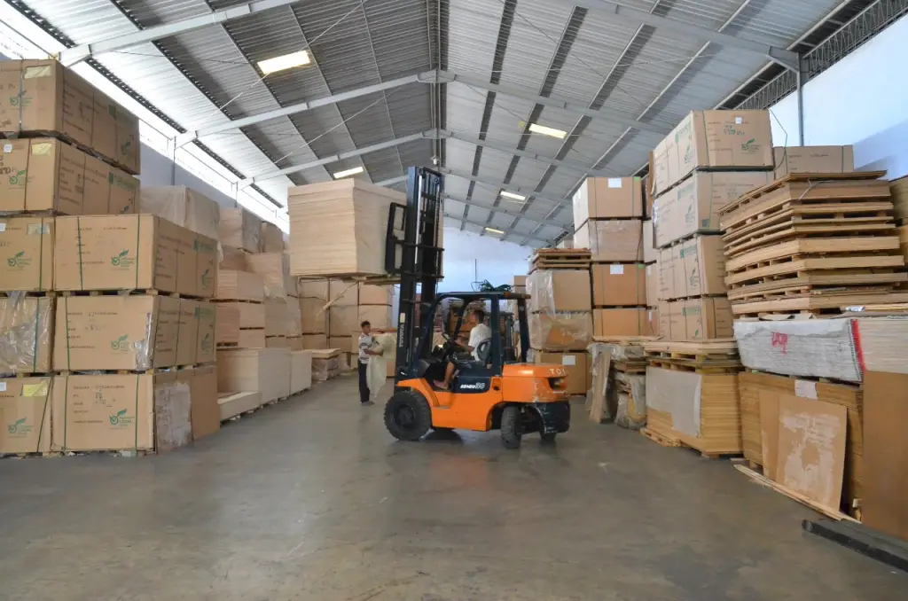 Gudang Indoho dengan forklift oranye sedang memuat stok triplek melamin dan plywood grosir siap kirim untuk area Semarang. Distributor kayu lapis terpercaya di Jawa Tengah
