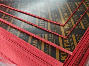 Close-up tumpukan Triplek Phenolic Film Face Kuda Hitam untuk bekisting cor, menunjukkan lapisan hitam dan pinggiran kedap air berwarna merah. Distributor resmi Indoho