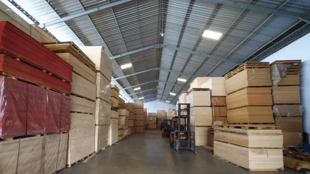 Gudang besar distribusi grosir plywood, MDF, Blockboard, dan material kayu lapis lainnya milik Indoho di Indonesia. Menunjukkan stok barang yang siap kirim dengan forklift. Supplier terpercaya