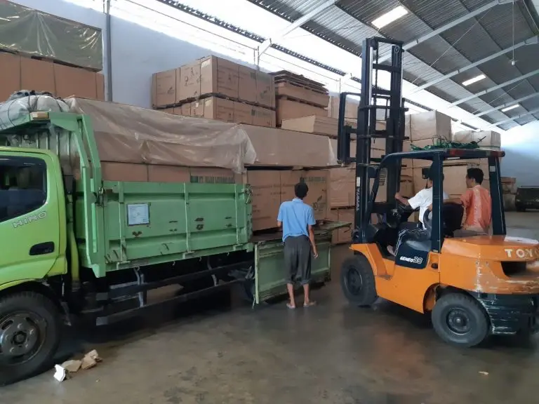 Forklift sedang memuat tumpukan kotak plywood ke atas truk kuning di gudang distributor PT Indoho Santosa Abadi Semarang.