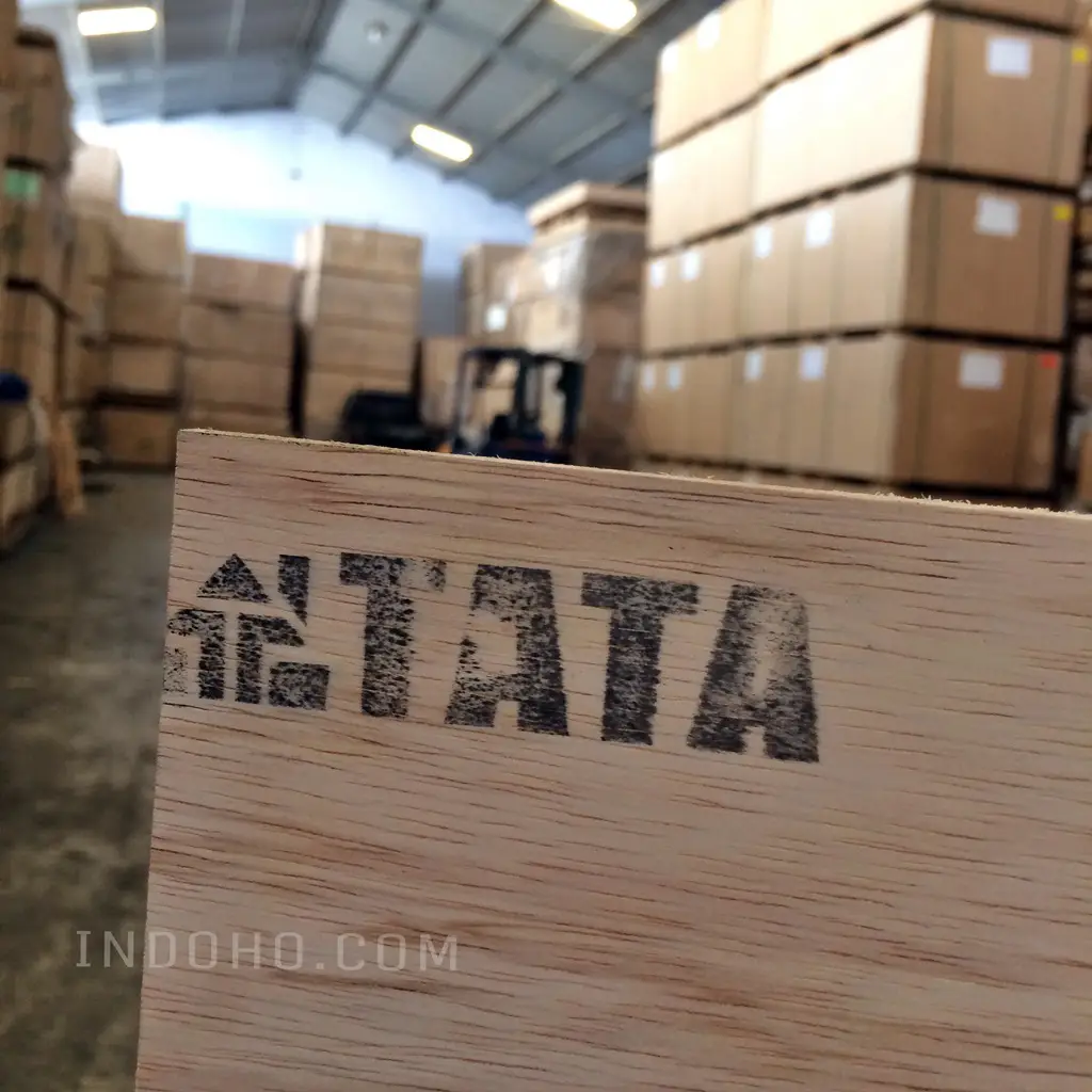 Tampilan dekat lembaran plywood multiplek bercap TATA berlatar belakang tumpukan stok kayu lapis dalam kapasitas besar di gudang distributor Indoho Semarang.